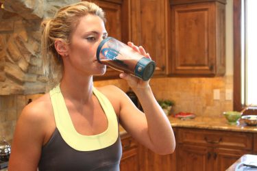 Mujer tomando batido de proteína - Fuente: Bodybuilding.com